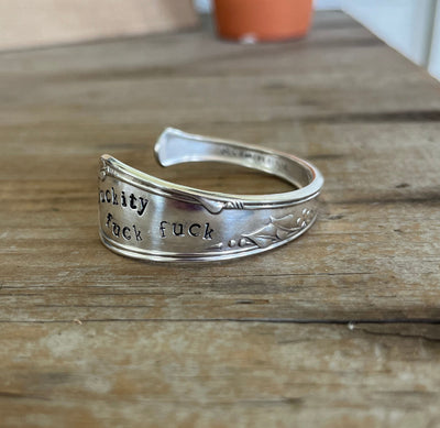 Close-up detail of FUCKITY FUCK FUCK hand-stamped on spoon cuff bracelet of Meadowbrook/Heather vintage silverplate pattern