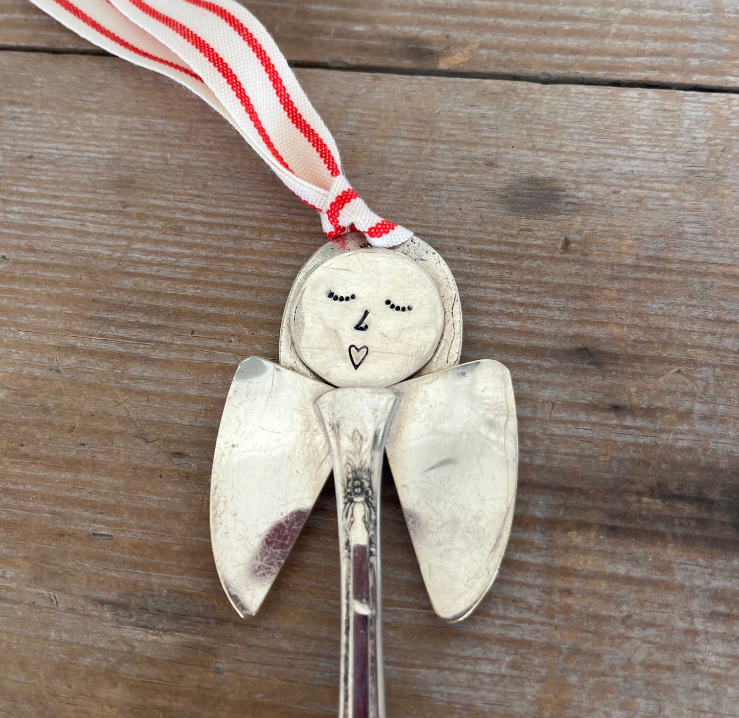 Close up of hand-stamped face of Frances artisan angel ornament with spoon handle body and spoon bowl wings with red striped ribbon hanger - handcrafted upcycled vintage silverware ornament - Laughing Frog Studio