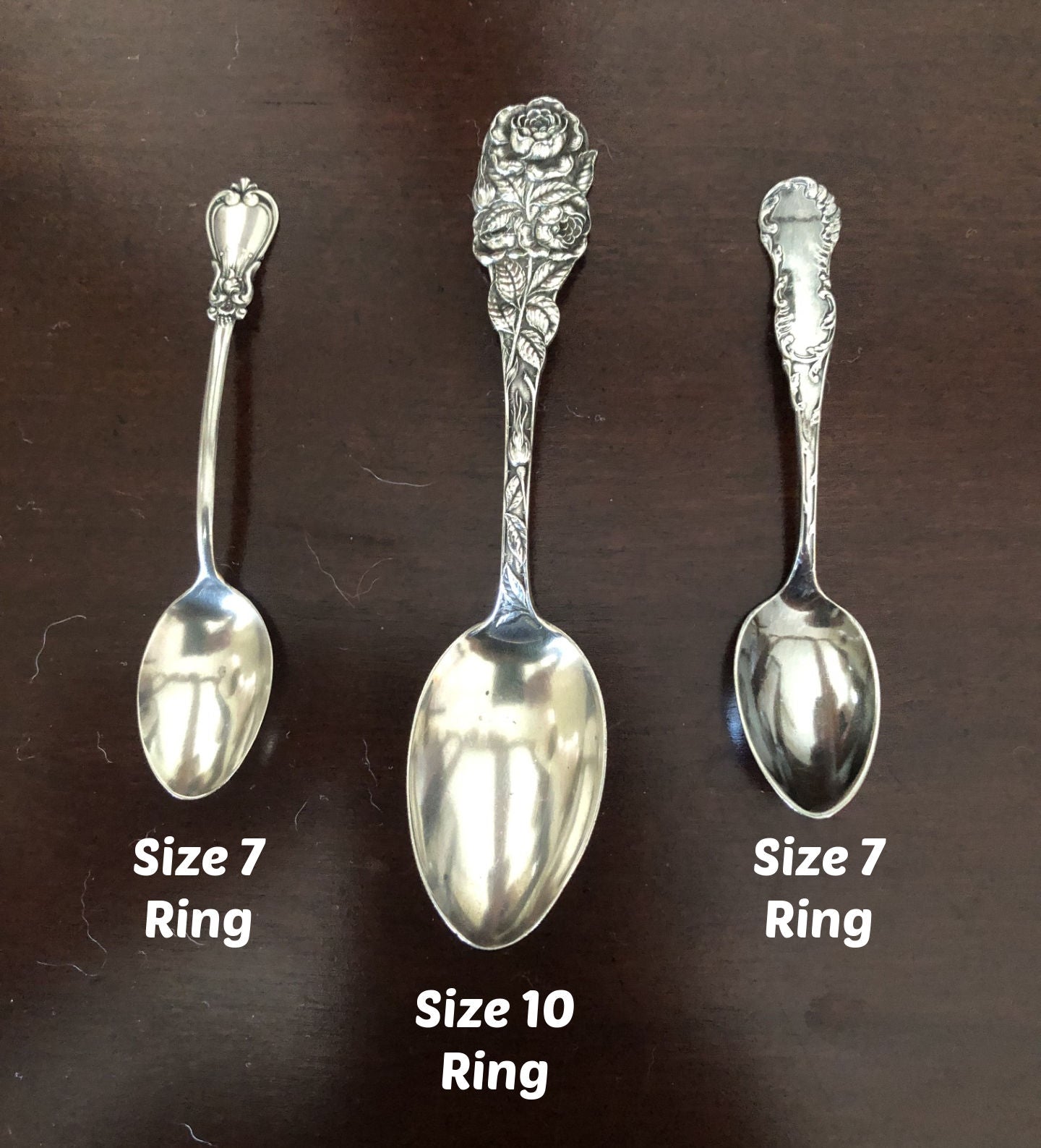 Three silver spoons with decorative handles on a dark brown background