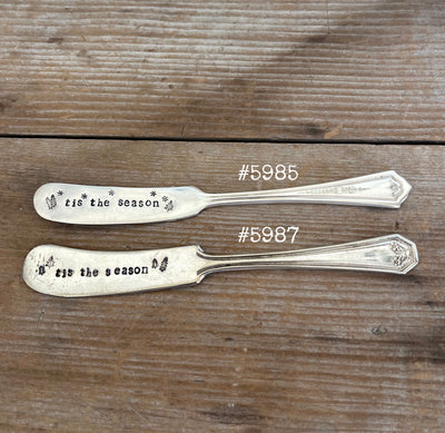 Two "tis the season" hand-stamped cheese spreaders flat lay on wood - hand-stamped cheese spreader - handcrafted from upcycled vintage silverware - Laughing Frog Studio