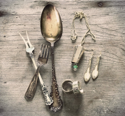 Ornate vintage spoons and forks laid next to upcycled spoon ring, earrings, and necklace — handcrafted silverware jewelry flat lay
