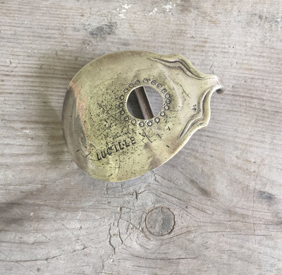Close-up of Lucille guitar spoon belt buckle showing hand-stamped circular ornamentation around sound hole, reclaimed vintage silverplate, one-of-a-kind
