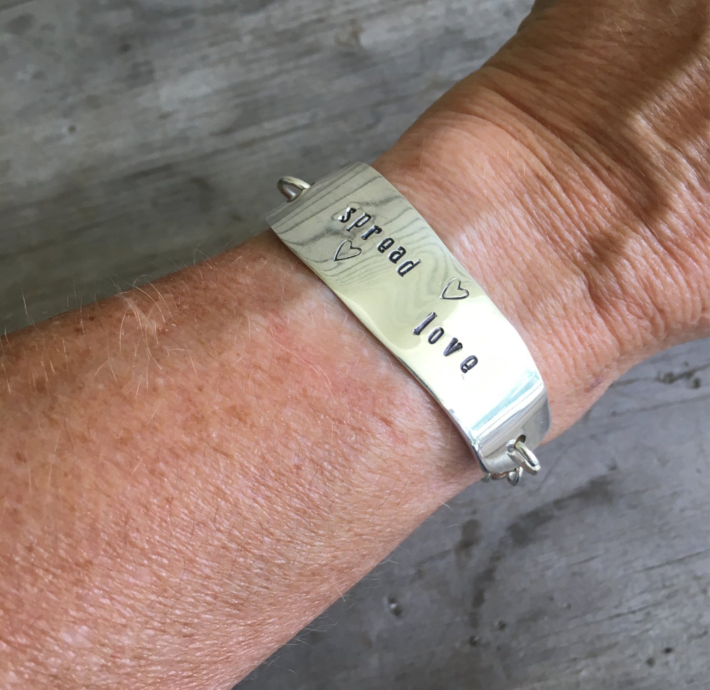 Spread Love stamped knife bracelet with heart charm modeled on wrist - handcrafted upcycled vintage silverware jewelry