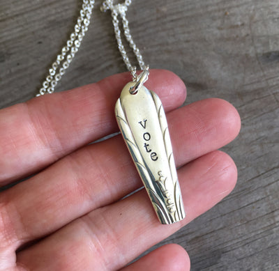 Close-up detail of VOTE bar pendant showing hand-stamped lettering and classic engraved urn with foliage, minimalist heirloom design, 21-inch chain