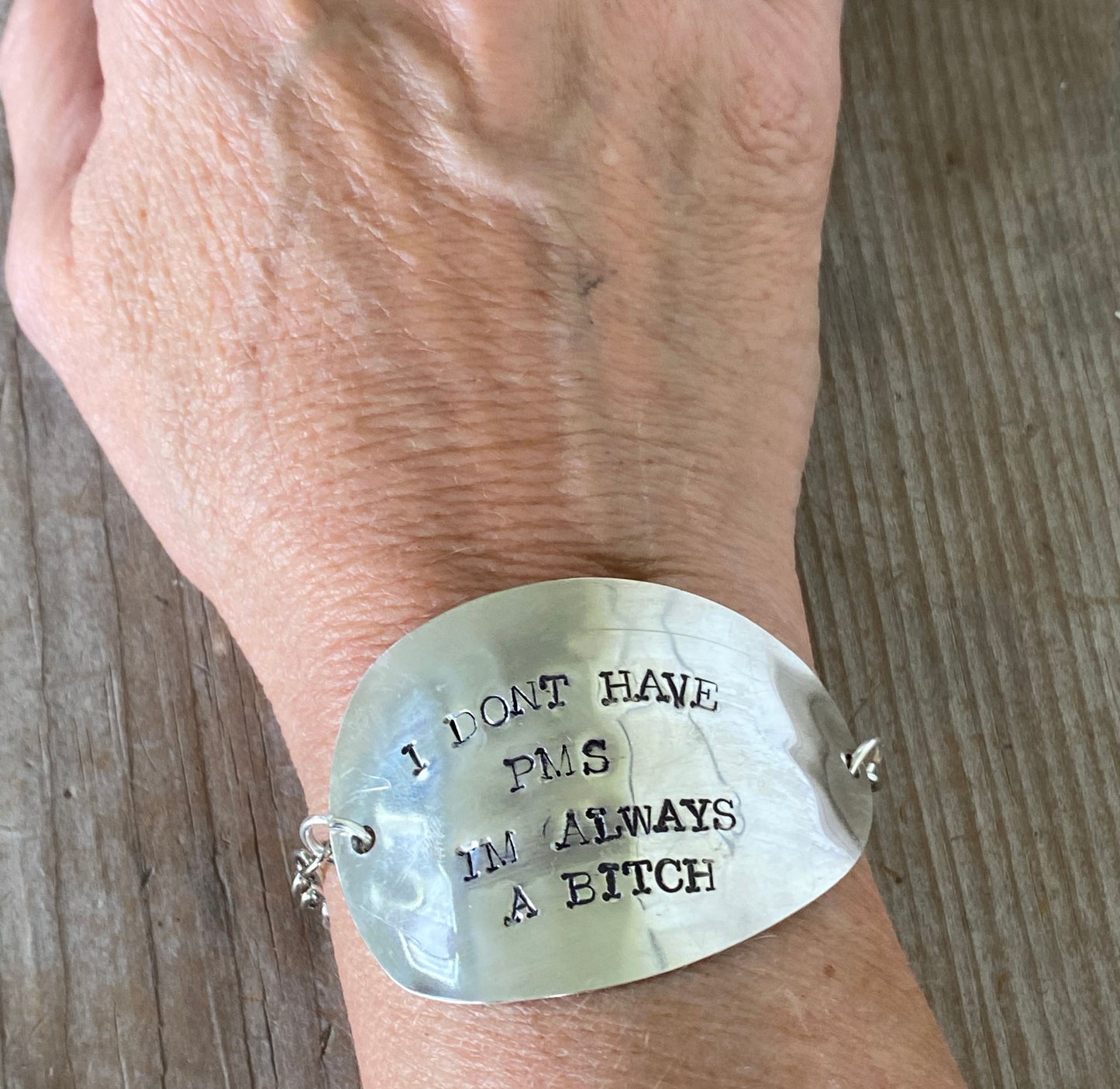 Upcycled silverware bracelet stamped with humorous PMS message worn on wrist, showing size and scale