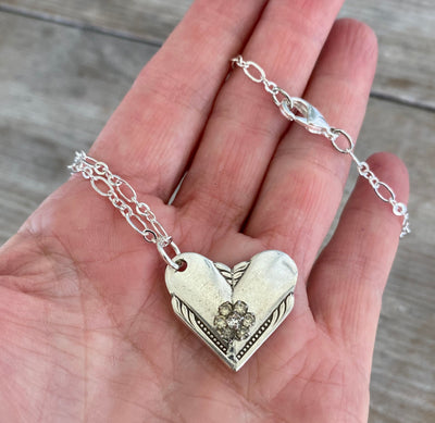 Close-up of Hiawatha spoon heart pendant showing vintage rhinestone earring flower detail, upcycled 1939 William Rogers silverware necklace - shown in hand for scale