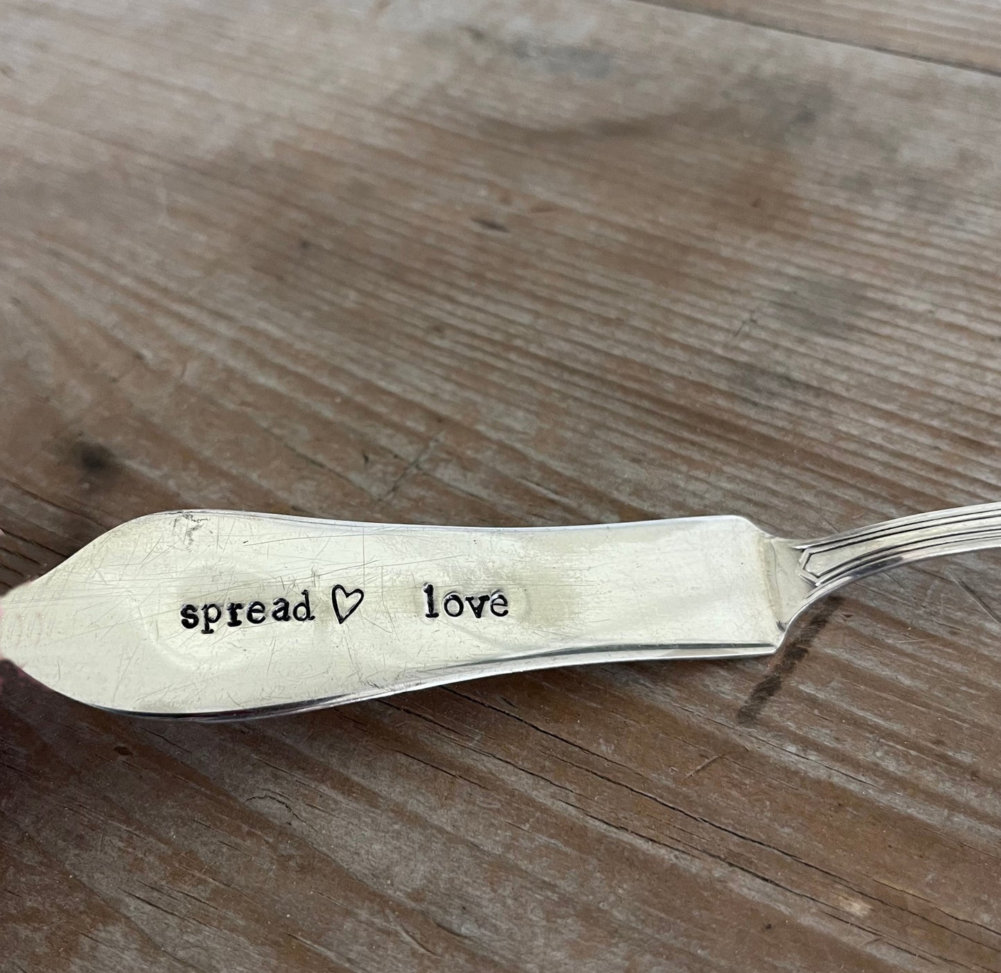 Close-up of SPREAD LOVE hand stamping on vintage silverware spreader knife