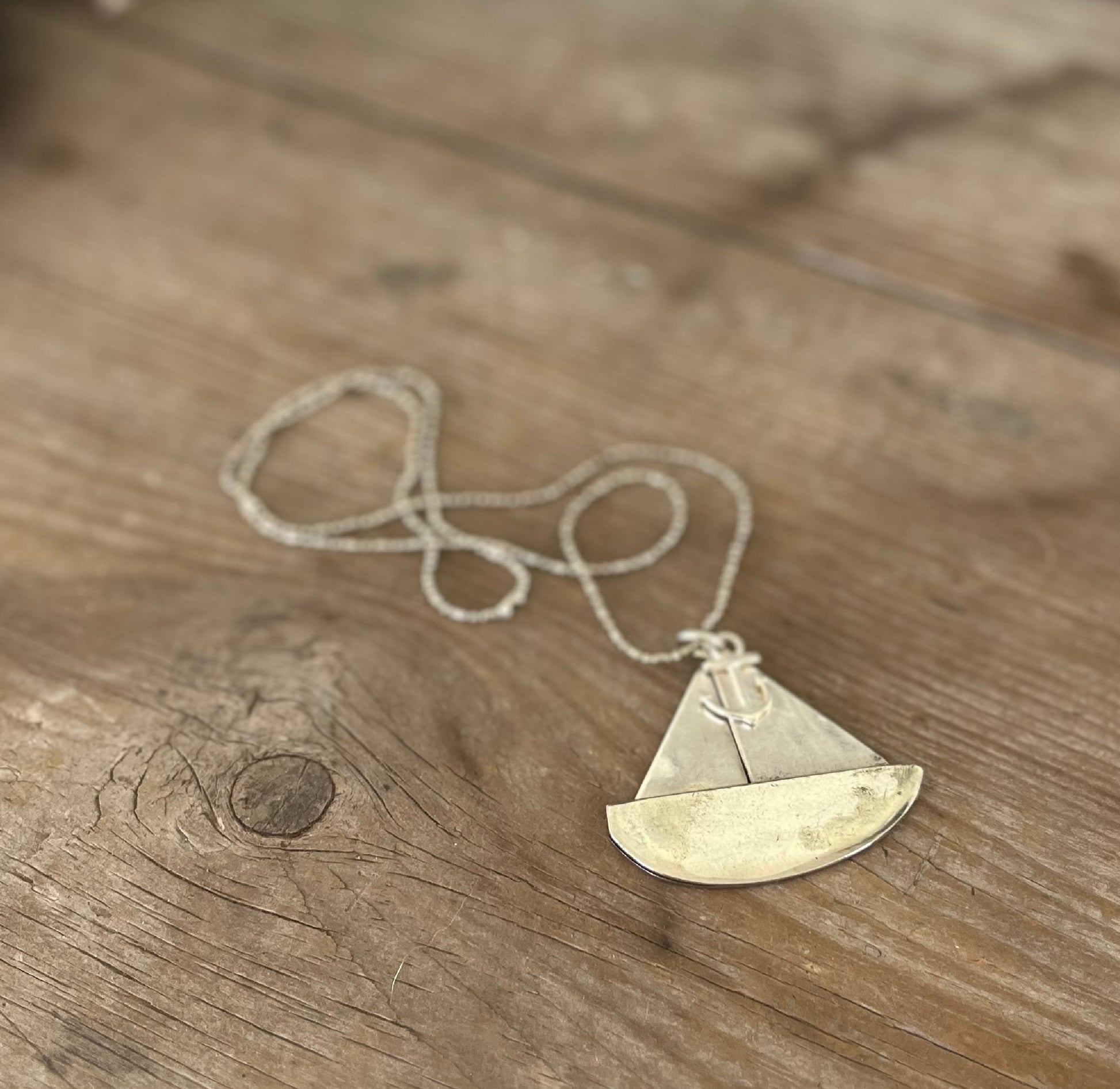 Close-up of vintage spoon sailboat pendant showing hand-stamped detail and anchor charm, sustainable artisan nautical jewelry