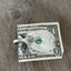 A vintage silver-plate sugar spoon money clip with a design resembling a guitar on the back, resting on a dollar bill.
