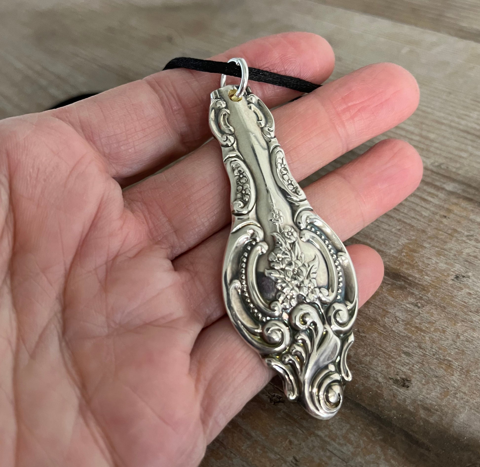 in hand view of large 3-inch vintage ladle handle pendant necklace showing depth and richness of Baroque silverplate design as well as size and scale