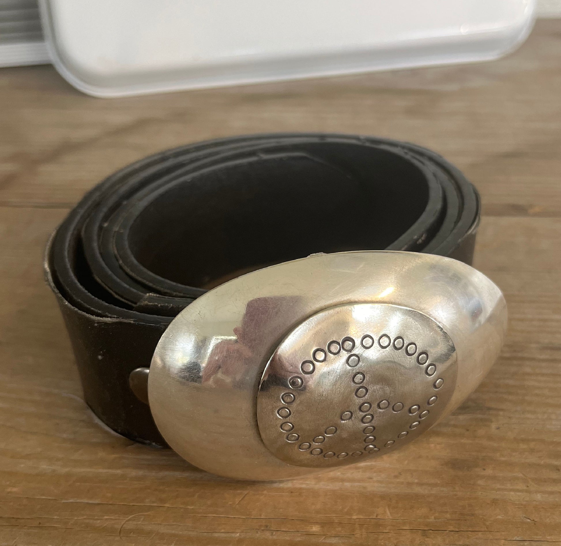 Close-up of PEACE belt buckle showing hand-stamped peace symbol on round bullion spoon applied to casserole spoon, one-of-a-kind silverplate