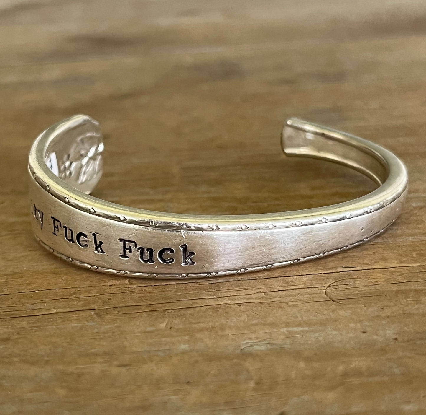 Silver spoon cuff bracelet from Prestige Silverplate Bordeaud pattern stamped fuckity fuck fuck on wood surface - cuff bracelet - handcrafted from upcycled vintage silverware - Laughing Frog Studio