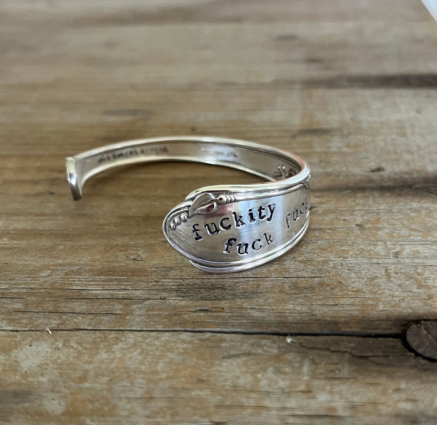 Shot of hand-stamping of FUCKITY FUCK FUCK on spoon cuff bracelet - 1936 William A. Rogers - upcycled vintage silverware - Laughing Frog Studio