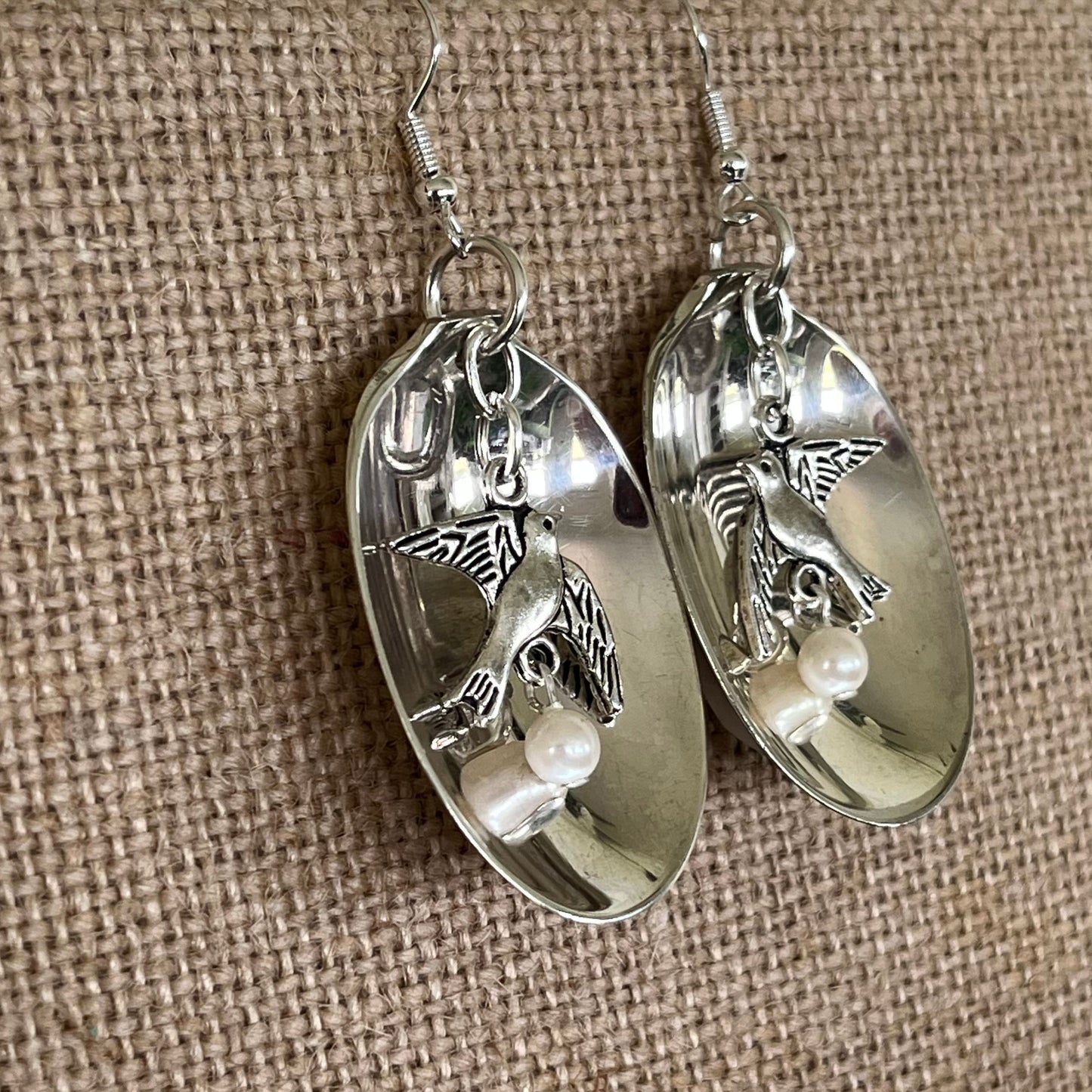 Close-up detail of baby food spoon bowl earrings with hanging bird charm and pearl bead, 2.375 inches long