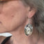 Baby food spoon earrings with bird of peace charms modeled on ear displaying wearable fit and charm detail