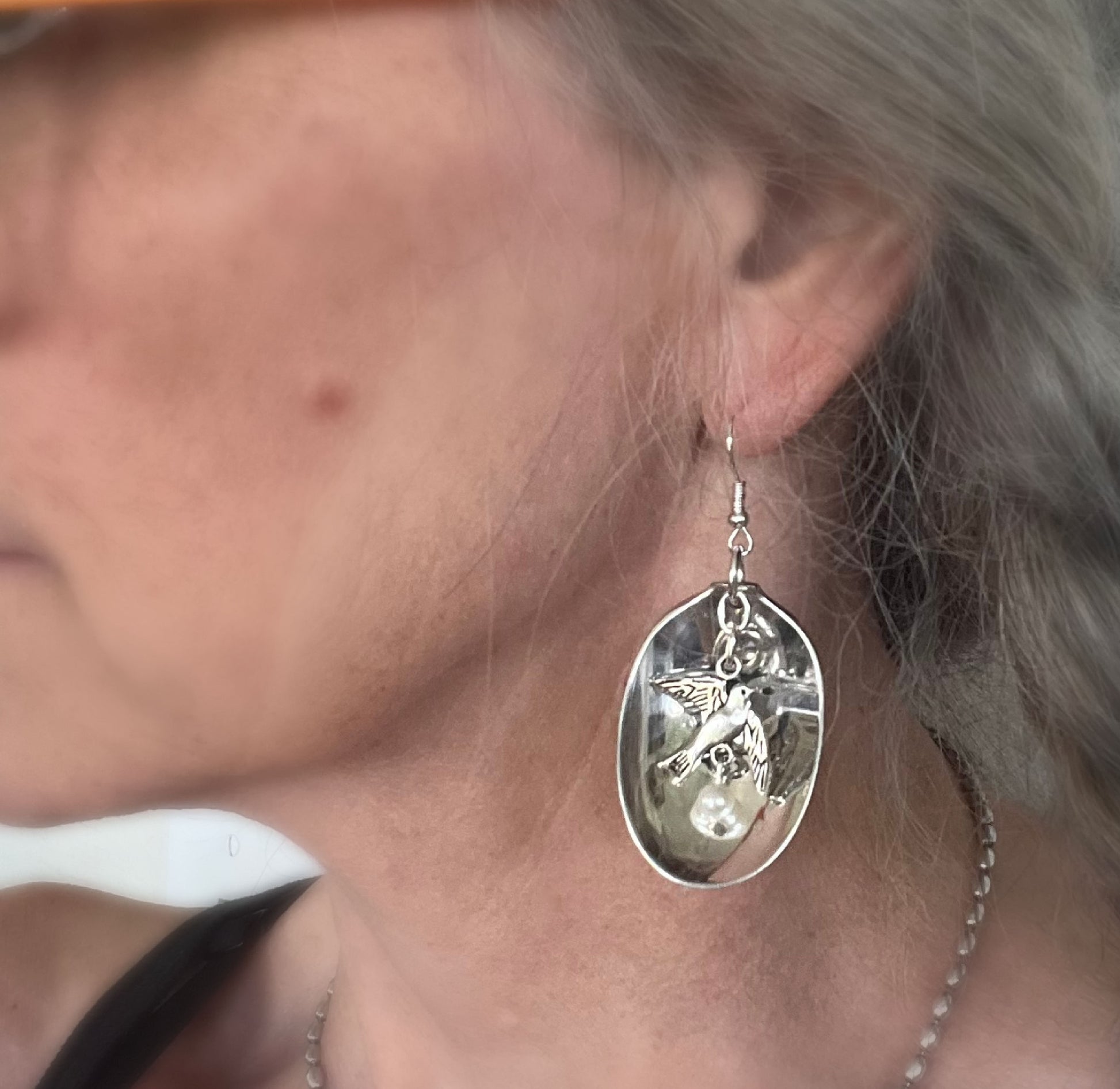 Baby food spoon earrings with bird of peace charms modeled on ear displaying wearable fit and charm detail