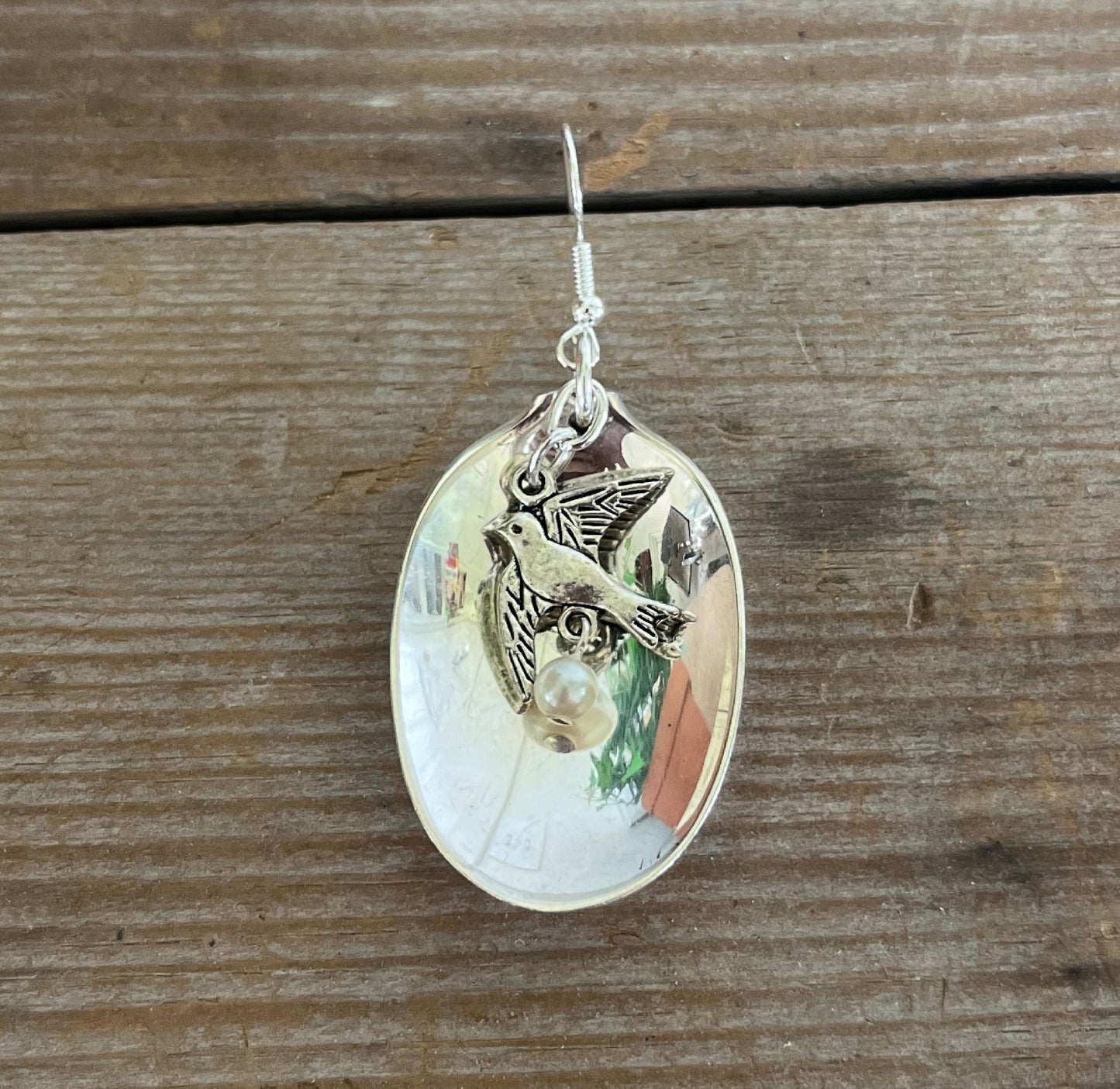 Detail view of vintage silverplate baby spoon earrings with dangling bird charm and faux pearl bead