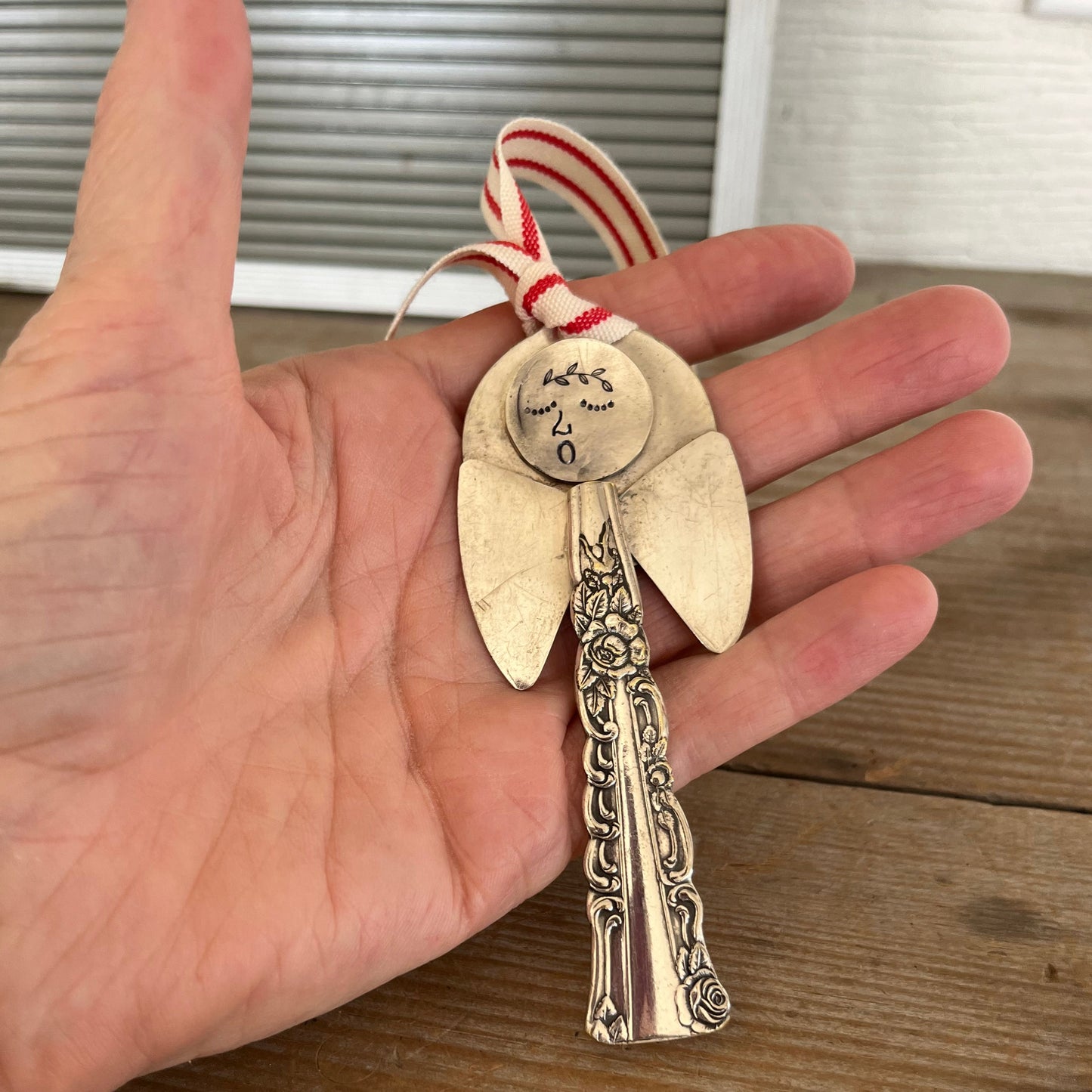 Minerva artisan angel ornament with spoon handle body and spoon bowl wings with red striped ribbon hanger shown in hand - handcrafted upcycled vintage silverware ornament - Laughing Frog Studio