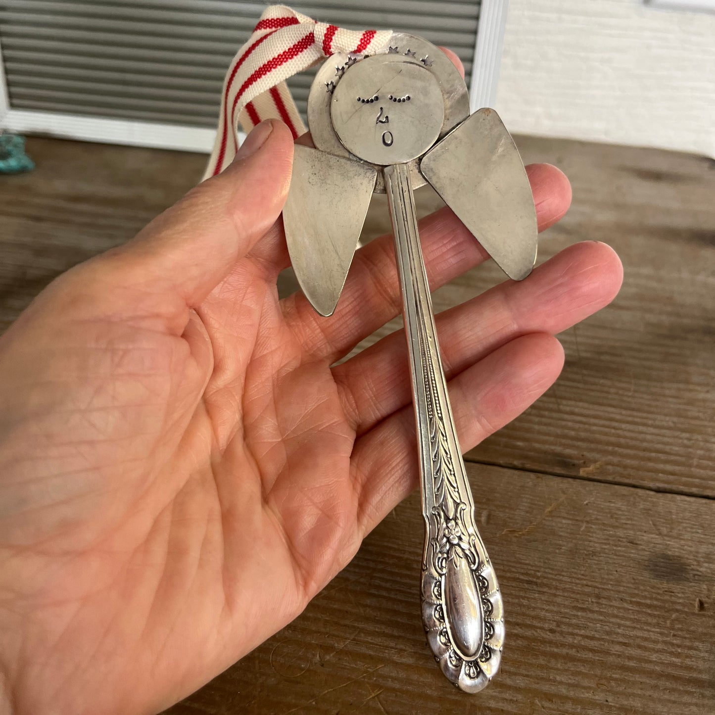 Hand holding Josephine pattern artisan angel ornament with spoon handle body and spoon bowl wings with red striped ribbon hanger - handcrafted upcycled vintage silverware ornament - Laughing Frog Studio