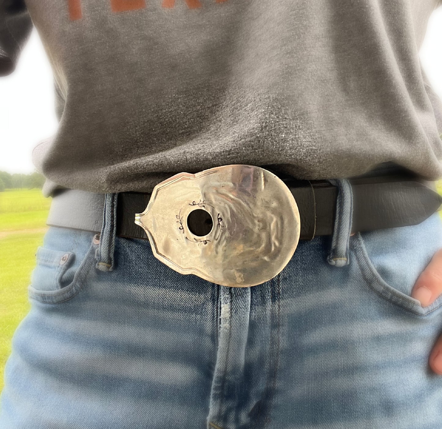 Close-up detail of handmade guitar spoon belt buckle showing hand-stamped scrollwork and drilled sound hole - upcycled vintage silverware - Laughing Frog Studio