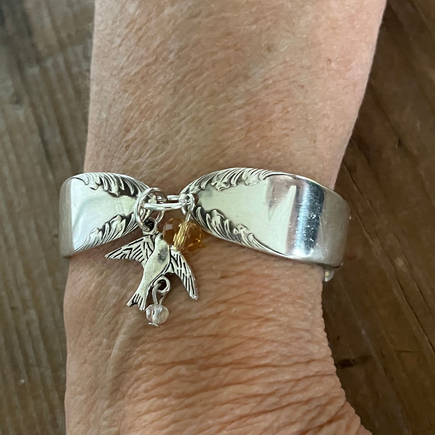 King Edward spoon link bracelet worn on wrist showing feathery scroll design and silver bird charm with golden crystal - handcrafted from upcycled vintage silverware - Laughing Frog Studio