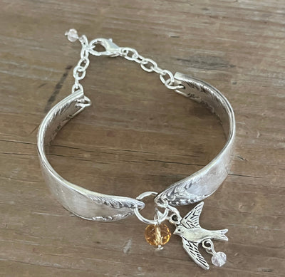 Top view of King Edward spoon link bracelet showing feathery scroll design, silver bird charm, golden crystal bead, and adjustable chain clasp - handcrafted from upcycled vintage silverware - Laughing Frog Studio