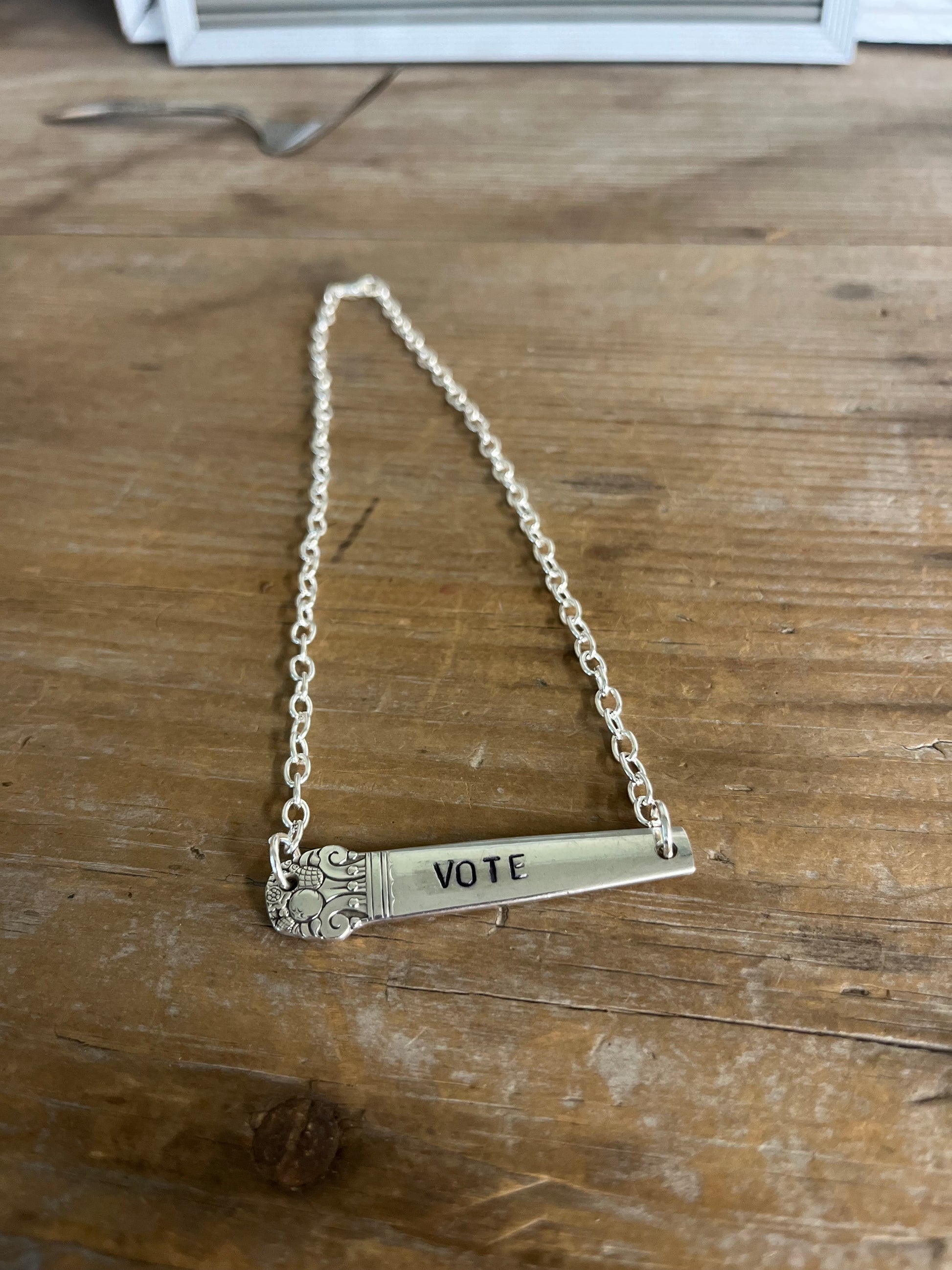 Wide shot of VOTE hand-stamped bar choker necklace laid flat on wood surface showing full chain length and vintage silverplate handle pendant - handcrafted from upcycled vintage silverware - Laughing Frog Studio