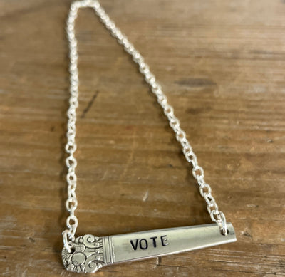 Flat lay of hand-stamped VOTE bar choker necklace showing full silver chain and vintage silverware handle pendant with floral graphic detail - handcrafted from upcycled vintage silverware - Laughing Frog Studio