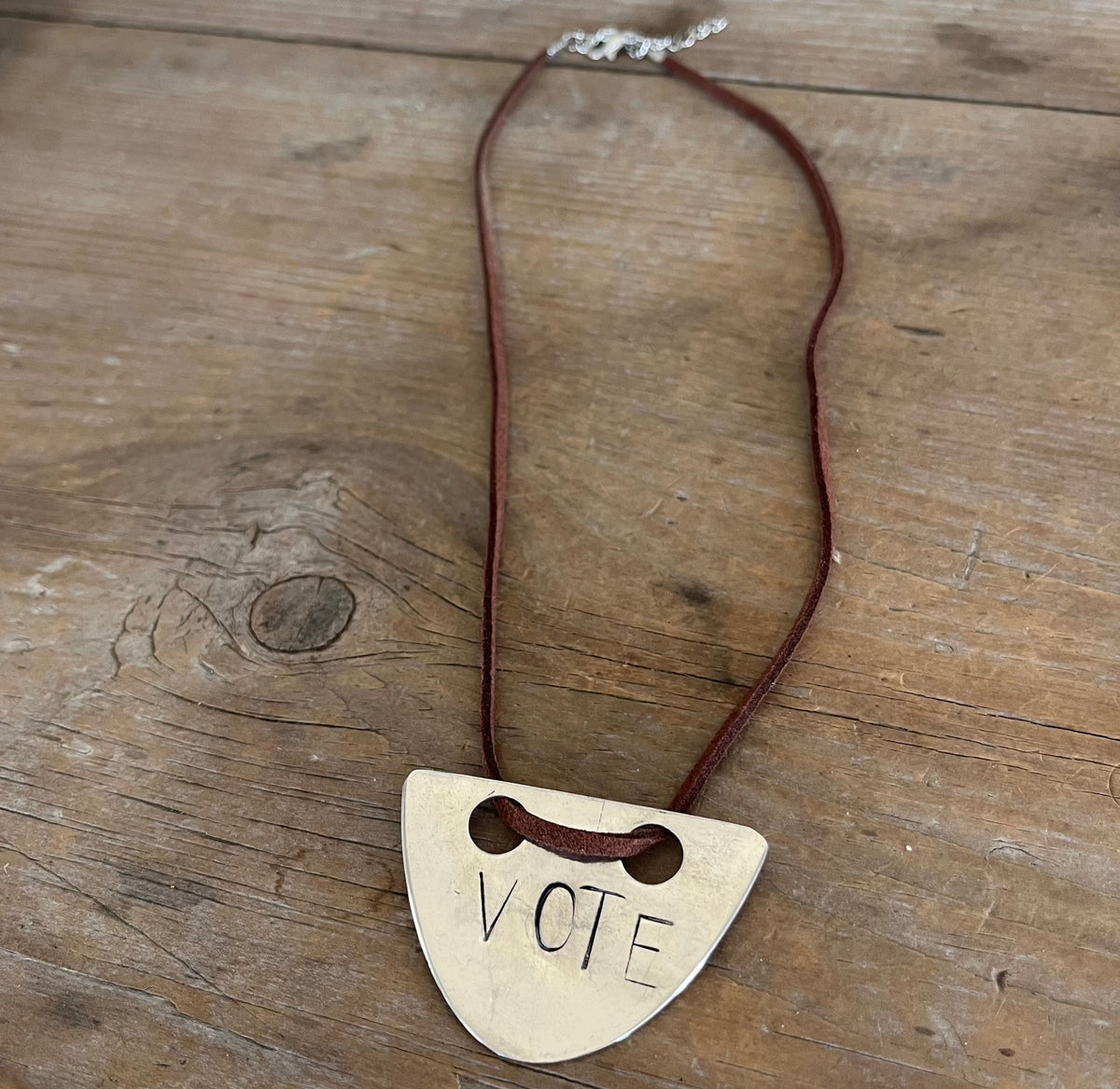 VOTE hand-stamped vintage spoon necklace on weathered wood showing full pendant and faux suede cord with metal links and clasp - upcycled silverware spoon necklace - handcrafted from upcycled vintage silverware - Laughing Frog Studio