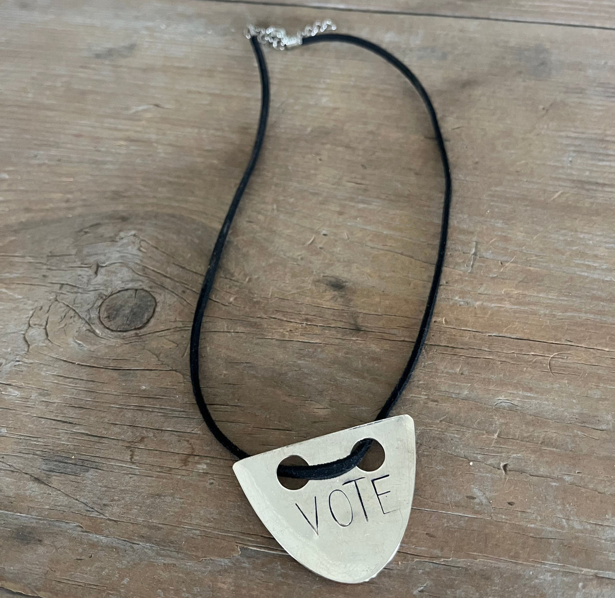 VOTE hand-stamped vintage spoon necklace on weathered wood showing full pendant and black faux suede cord with metal clasp - upcycled silverware spoon necklace - handcrafted from upcycled vintage silverware - Laughing Frog Studio