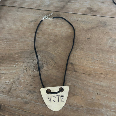 VOTE hand-stamped vintage spoon necklace on wood table showing full pendant and black faux suede cord with adjustable metal clasp - upcycled silverware spoon necklace - handcrafted from upcycled vintage silverware - Laughing Frog Studio