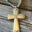 Spoon cross pendant on a silverplate bead choker with turquoise-colored accent beads, resting on weathered wood.
