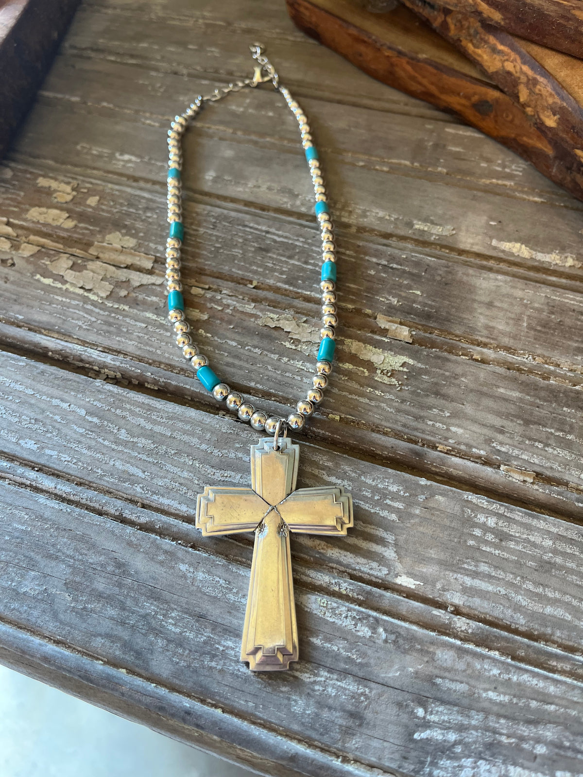 Full silverplate bead choker with turquoise-colored accent beads, spoon cross pendant, and clasp, laid flat on wood.