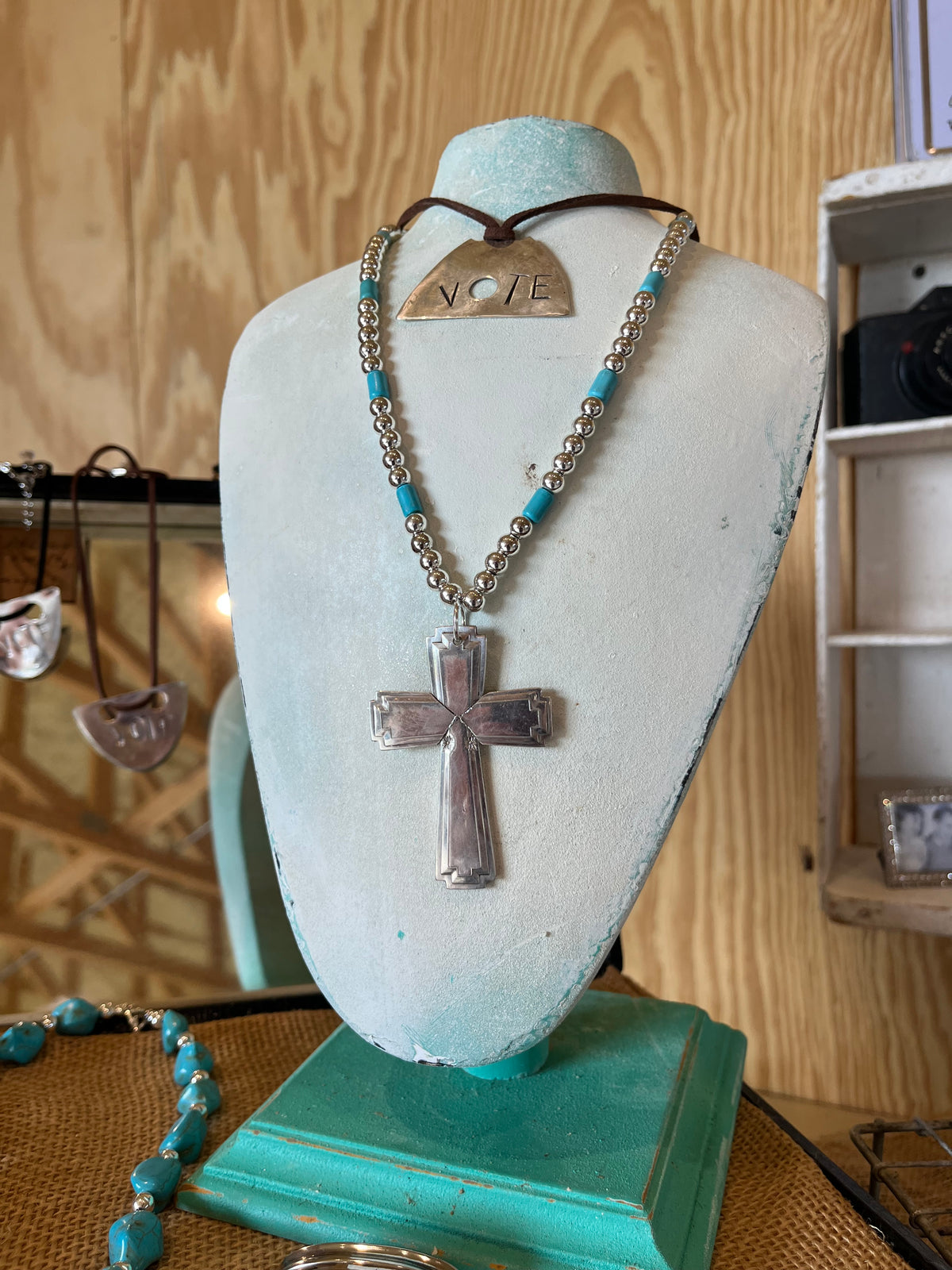 poon cross pendant and silverplate bead choker with turquoise-colored accents on a necklace display bust