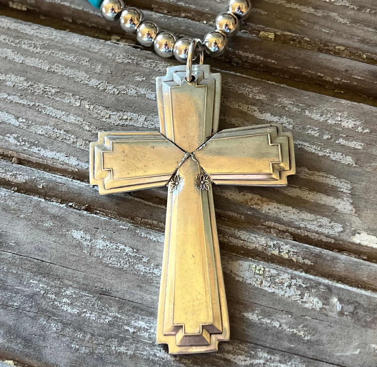 Close-up of spoon cross pendant with stepped borders and small floral details on a silverplate bead choker.