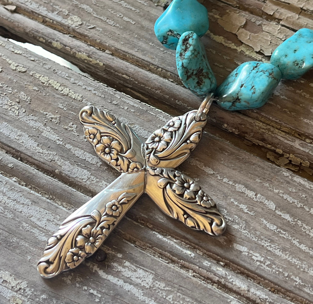Close-up of Evening Star floral spoon-handle cross pendant with turquoise howlite beads on rustic wood - Spoon cross choker necklace - handcrafted from upcycled vintage silverware - Laughing Frog Studio