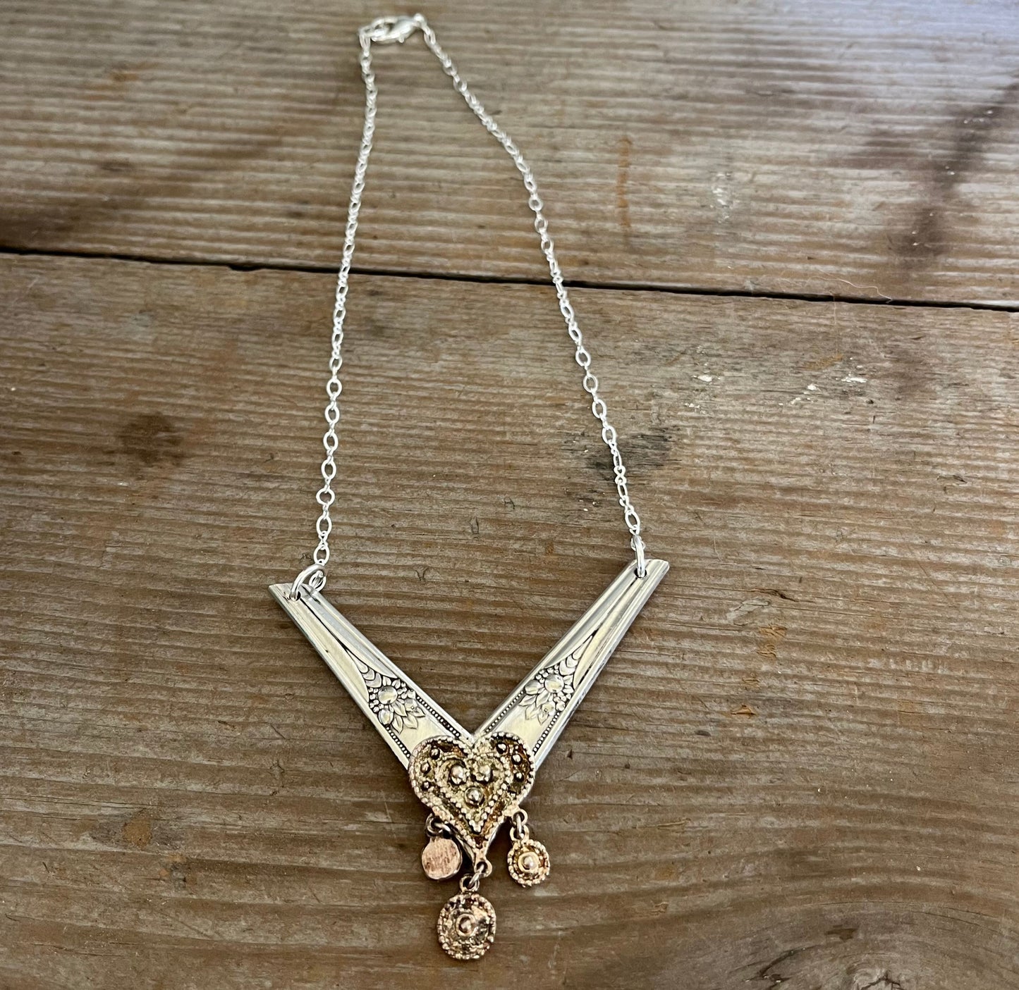 Close-up of chevron spoon pendant showing vintage earring heart accent at point, handcrafted silverware choker necklace detail