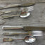 Rows of mixed vintage hand-stamped custom silverplate flatware sets with knives forks and spoons flat lay on wood - vintage silverware - handcrafted from upcycled vintage silverware - Laughing Frog Studio