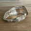 Side photo of William Rogers & Son Orange Blossom pattern spoon cuff bracelet with ornate floral repousse pattern on weathered wood - handcrafted upcycled vintage silverware cuff - Laughing Frog Studio