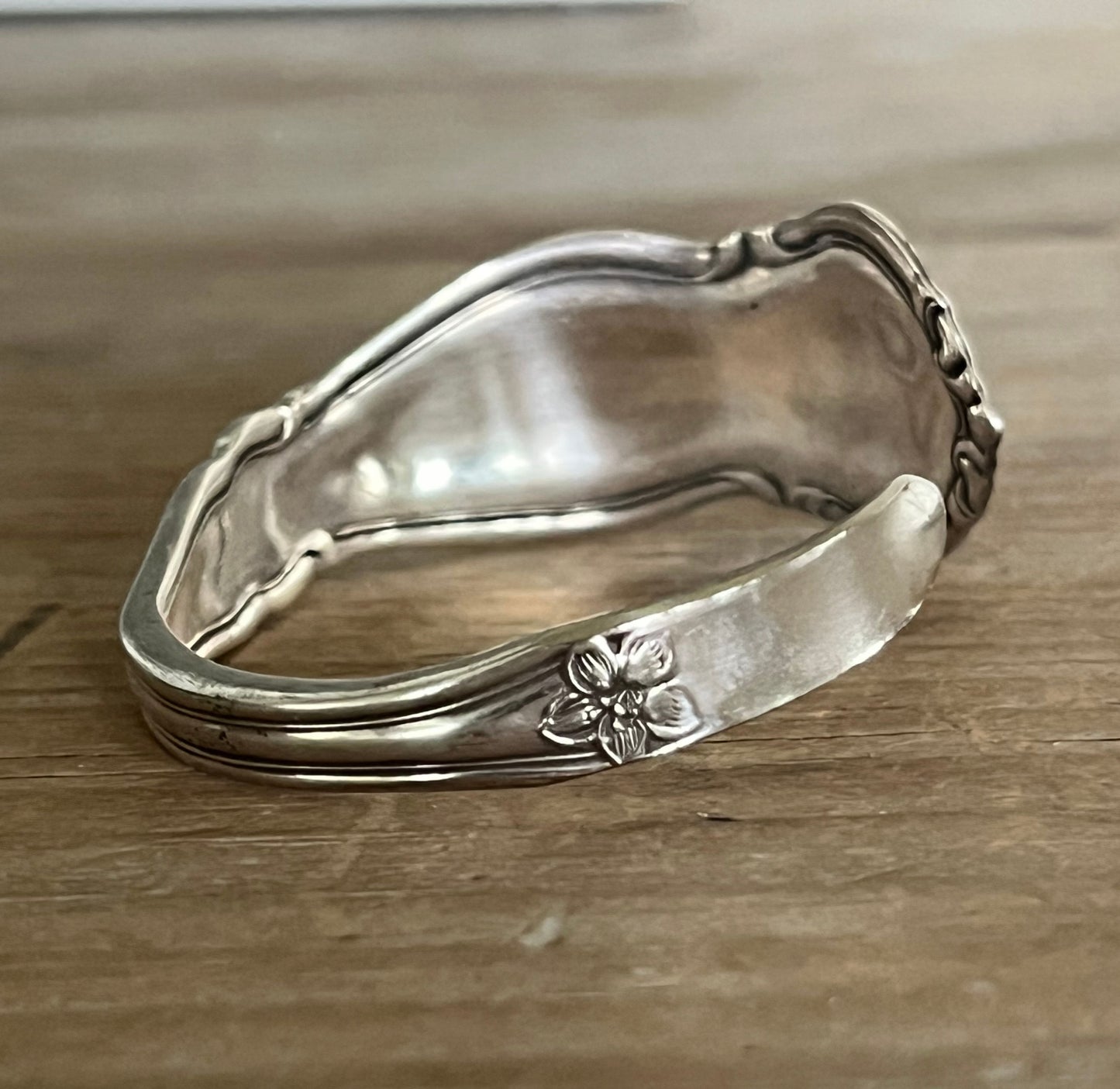 Side photo of William Rogers & Son Orange Blossom pattern spoon cuff bracelet with ornate floral repousse pattern on weathered wood - handcrafted upcycled vintage silverware cuff - Laughing Frog Studio