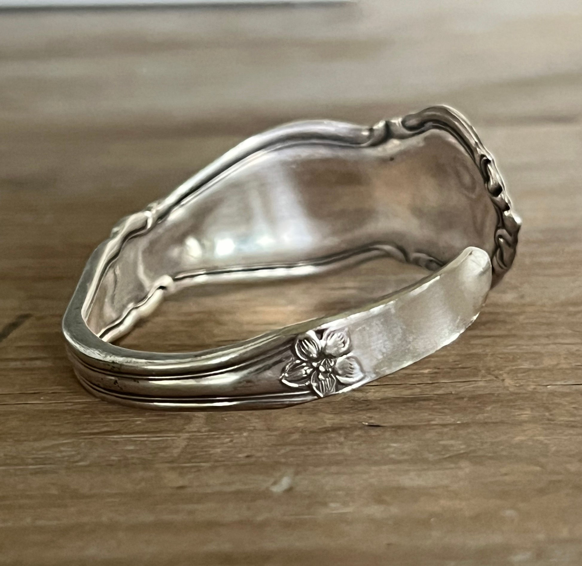 Side photo of William Rogers & Son Orange Blossom pattern spoon cuff bracelet with ornate floral repousse pattern on weathered wood - handcrafted upcycled vintage silverware cuff - Laughing Frog Studio