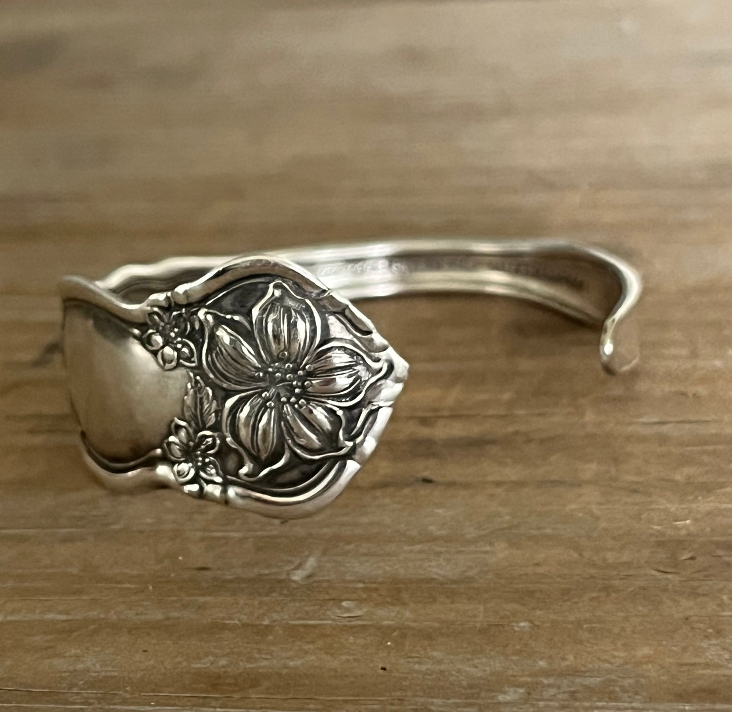 Detailed photo of William Rogers & Son Orange Blossom pattern spoon cuff bracelet with ornate floral repousse pattern on weathered wood - handcrafted upcycled vintage silverware cuff - Laughing Frog Studio