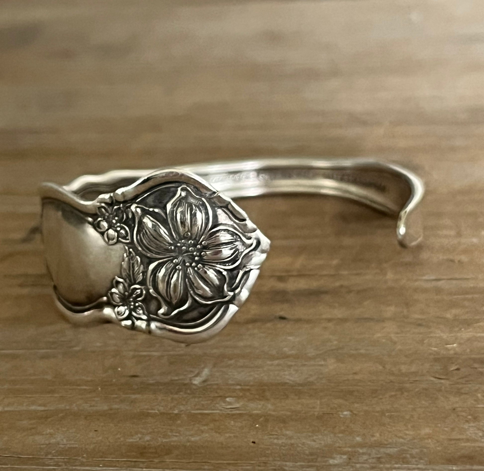 Detailed photo of William Rogers & Son Orange Blossom pattern spoon cuff bracelet with ornate floral repousse pattern on weathered wood - handcrafted upcycled vintage silverware cuff - Laughing Frog Studio
