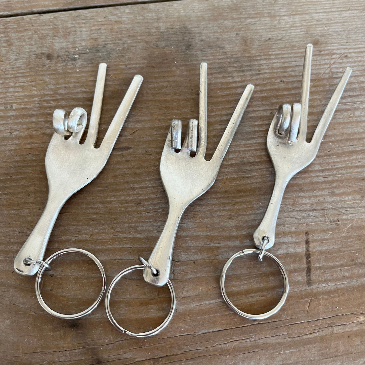 Collection of three Handmade peace sign keychains from upcycled vintage forks with two-finger hand gesture