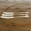 Side view of three "Spread Cheer" hand-stamped cheese spreaders comparison flat lay on wood - handcrafted from upcycled vintage silverware - Laughing Frog Studio