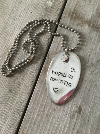 Close-up of HOPELESS ROMANTIC hand-stamped spoon pendant with decorative jewel showing love-inspired message on reclaimed vintage silverware