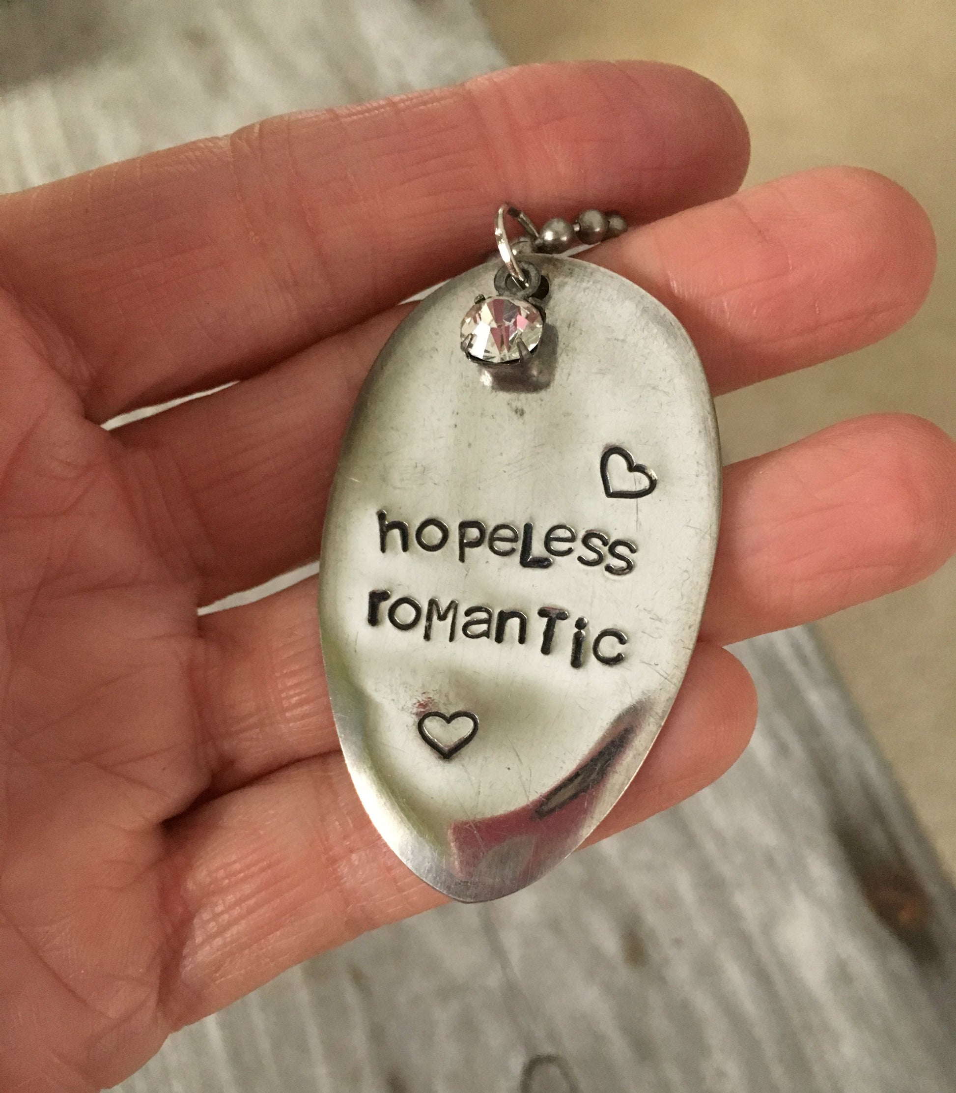 HOPELESS ROMANTIC hand-stamped spoon necklace with jewel held in hand for scale showing one-of-a-kind romantic design on vintage ball chain