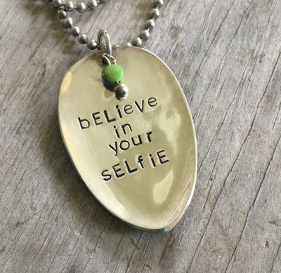 Close-up of BELIEVE IN YOUR SELFIE hand-stamped spoon pendant with playful beads showing confident message on reclaimed vintage silverware, 16-inch chain