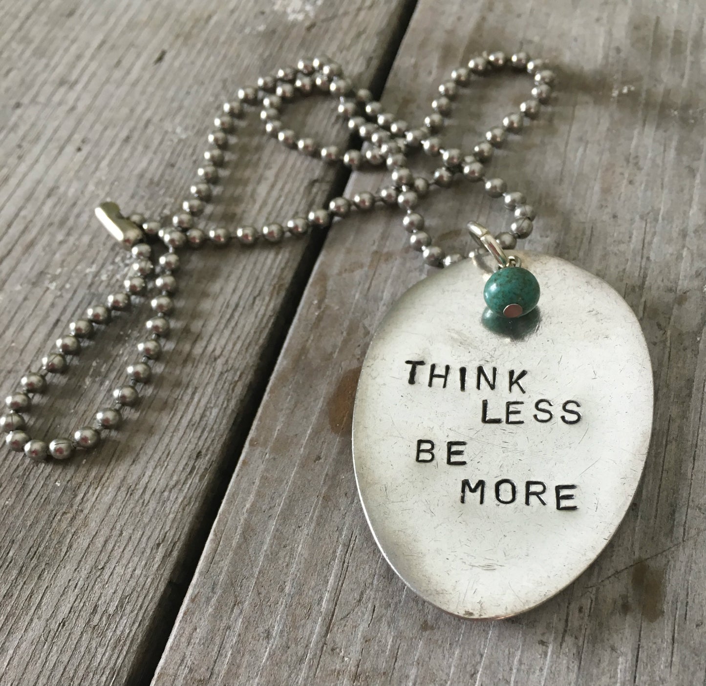 Close-up of THINK LESS BE MORE hand-stamped spoon pendant with turquoise bead showing inspirational motto on reclaimed vintage silverware