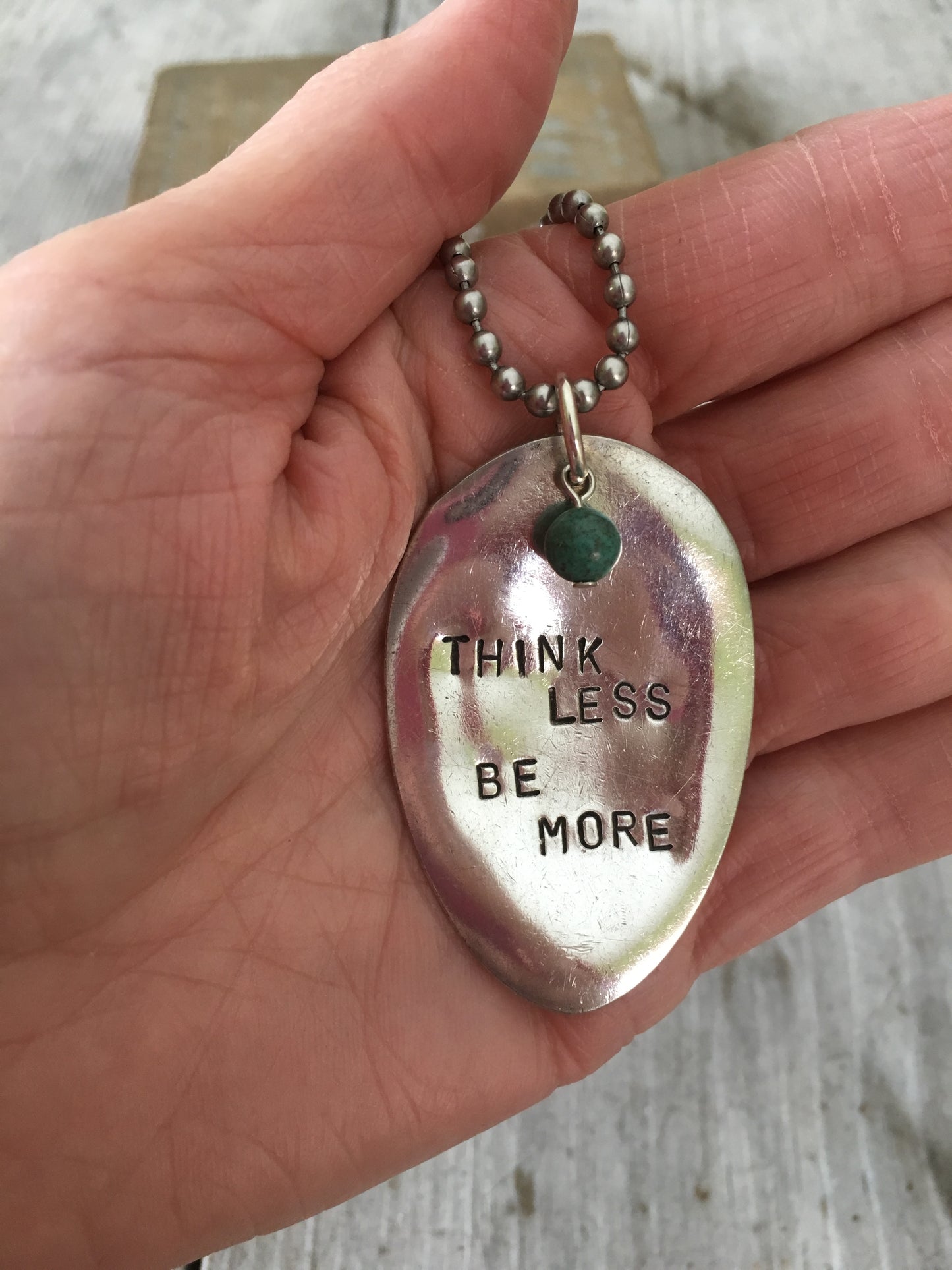 THINK LESS BE MORE hand-stamped spoon necklace with turquoise stone bead held in hand for scale, layerable gypsy style motivational jewelry